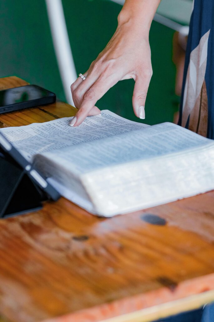Person reading religious book at table with a digital device, combining tradition and technology.